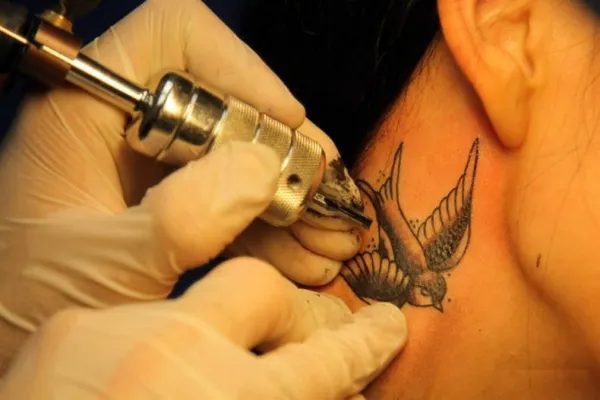 татуировщик набивает ласточку на шее