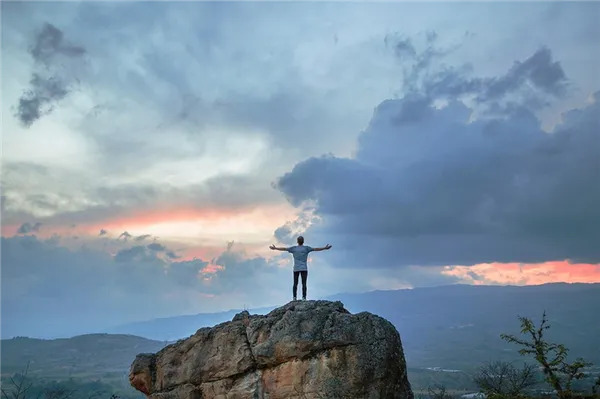 Мужчина стоит на вершине горы, раскинув руки в стороны